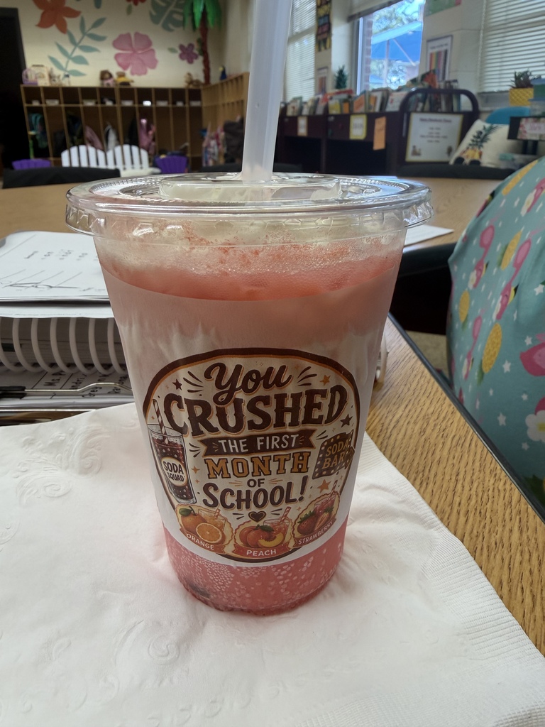 A close-up of a pink-colored beverage in a clear cup with a “You Crushed the First Month of School” label. The label features soda-themed illustrations and orange, peach, and strawberry flavor images.