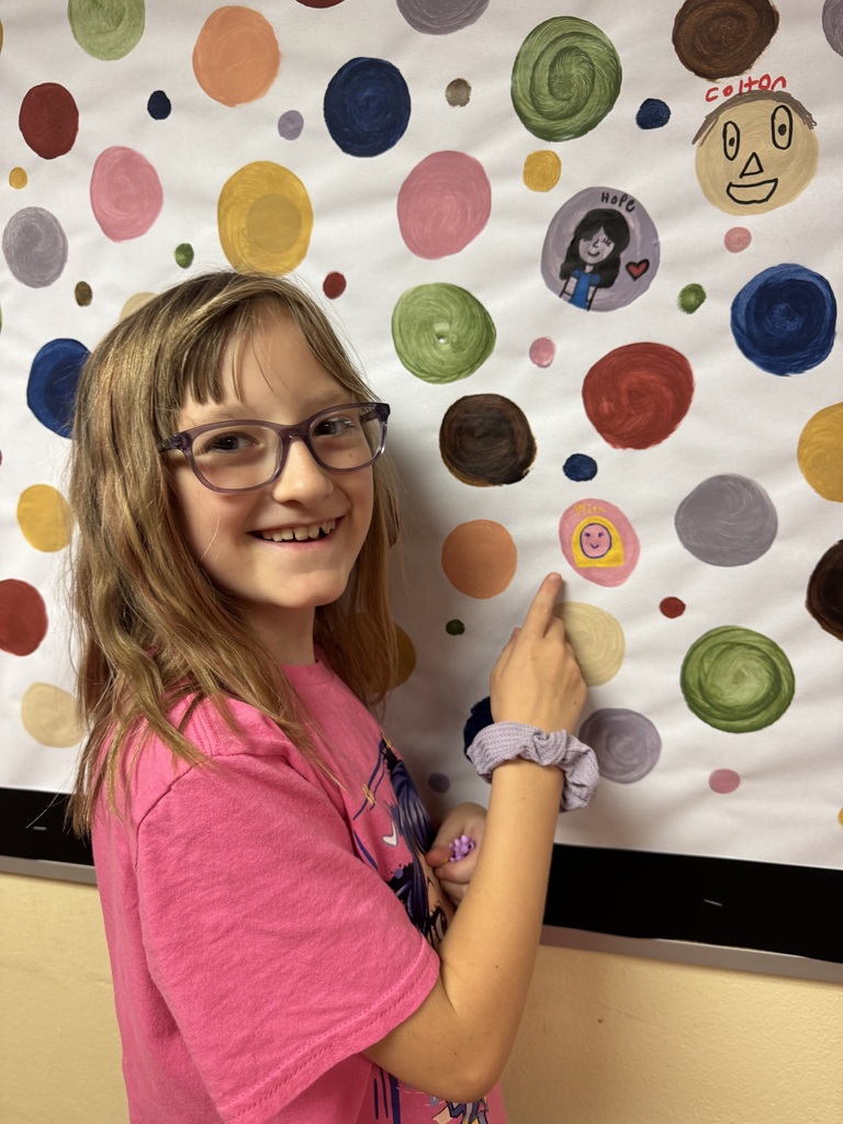 A student proudly point to their dots representing our school-wide expectations. The student smiles as she shows her commitment to making positive choices at school.