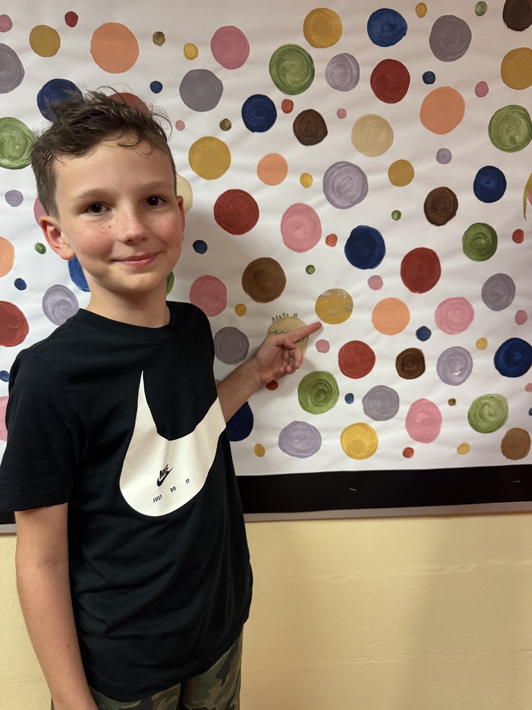 A student proudly point to their dots representing our school-wide expectations. The student smiles as he shows his commitment to making positive choices at school.