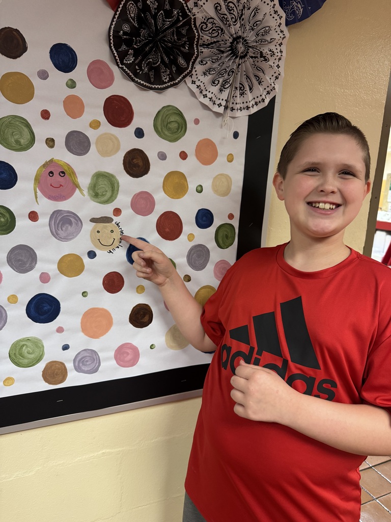 A student proudly point to their dots representing our school-wide expectations. The student smiles as he shows his commitment to making positive choices at school.