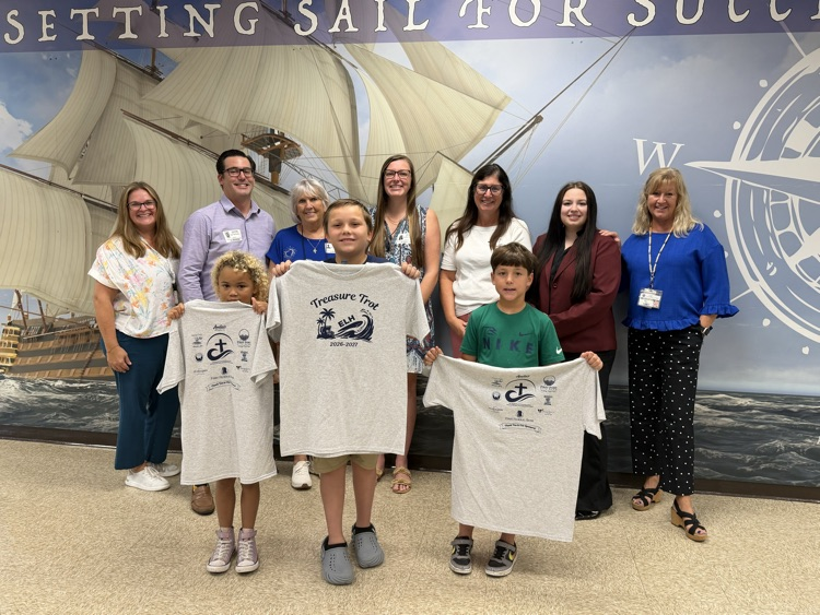 several adults smiling standing behind 3 students.  2 students are holding a Fun Rin t-shirt and one student is showing the back of the t-shirt