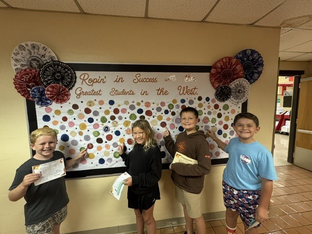 Students proudly point to their dots representing our school-wide expectations: Be Respectful, Be Responsible, and Be Safe. The students smile as they show their commitment to making positive choices at school.