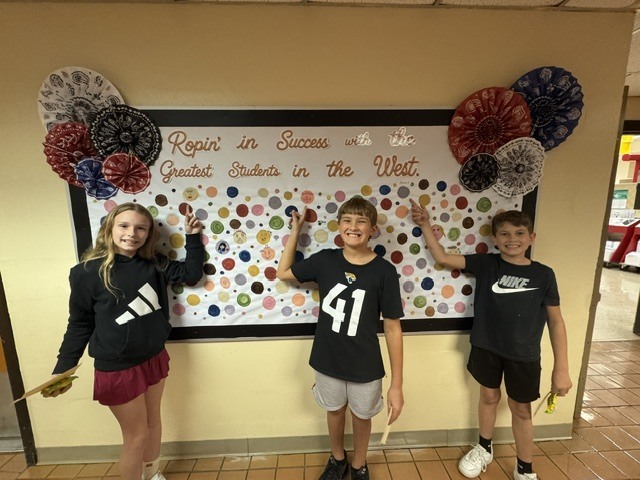 Students proudly point to their dots representing our school-wide expectations: Be Respectful, Be Responsible, and Be Safe. The students smile as they show their commitment to making positive choices at school.