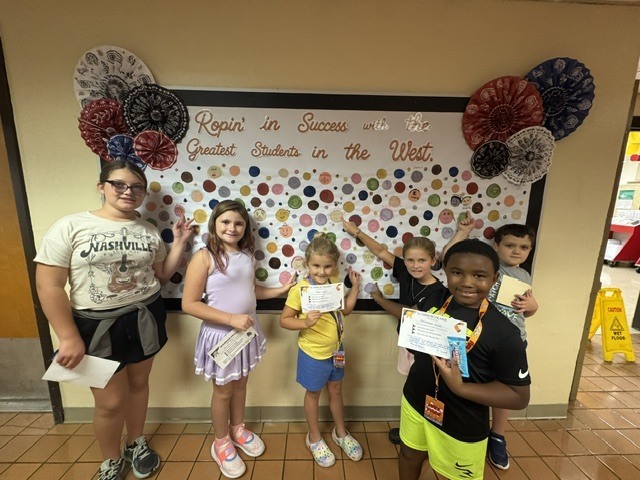 Students proudly point to their dots representing our school-wide expectations: Be Respectful, Be Responsible, and Be Safe. The students smile as they show their commitment to making positive choices at school.