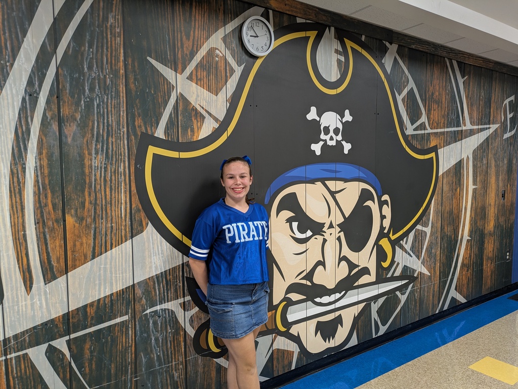 Young pirate cheerleader standing next to a pirate mural on a wall.