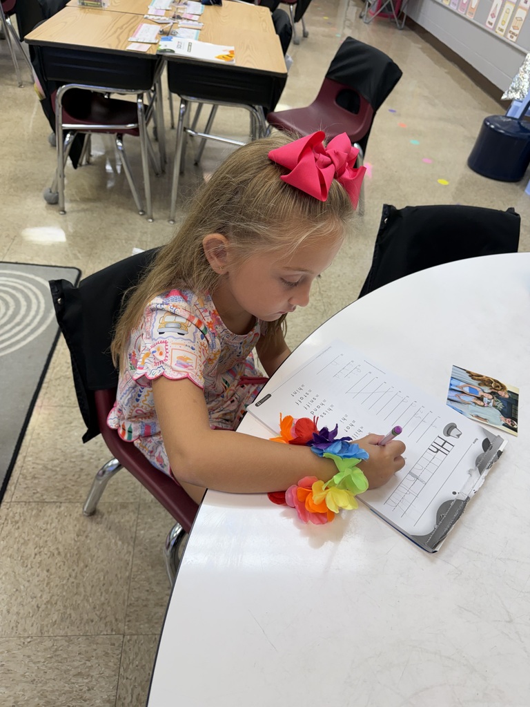 student in a pink hair bow working at a table