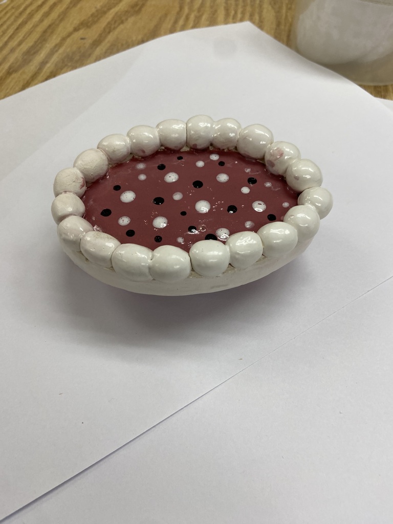 Student ceramics sample: White ceramic bowl with a pink center decorated with black and white dots and a rim of rounded white beads.