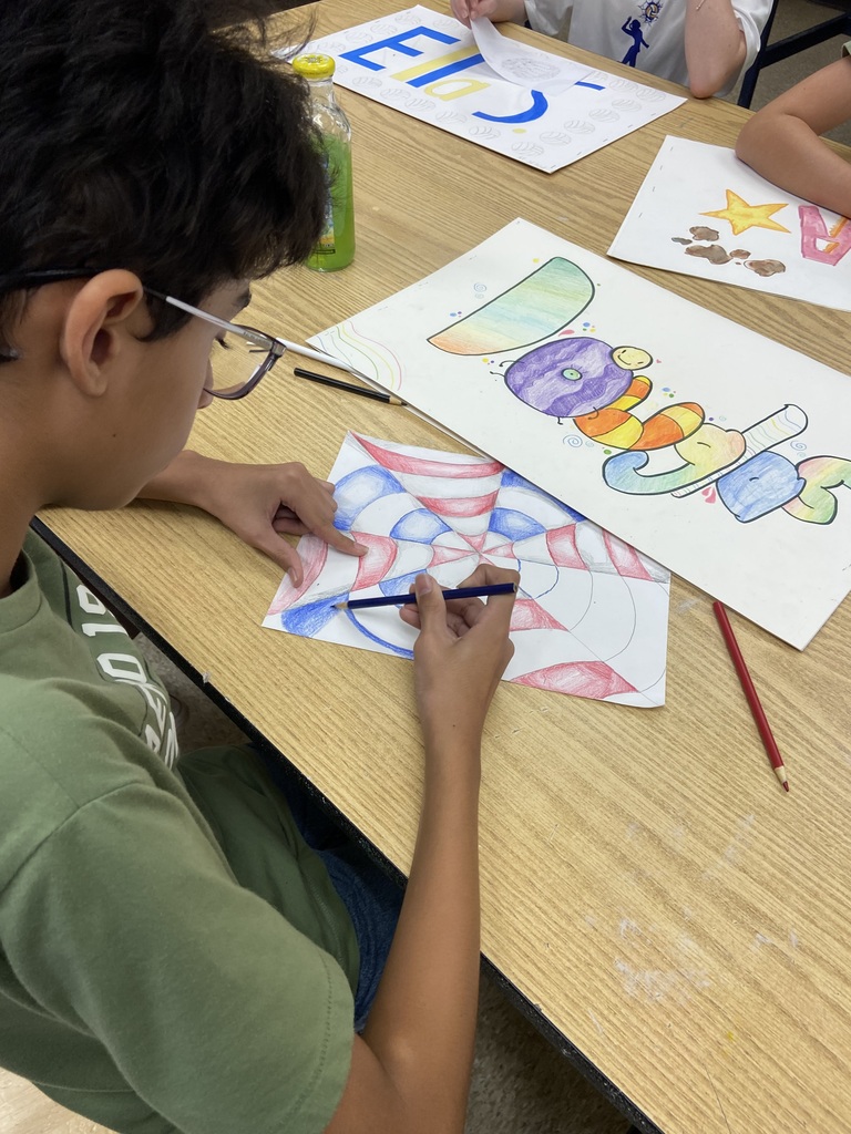 Student coloring a geometric optical illusion design with red and blue colored pencils at a classroom table.