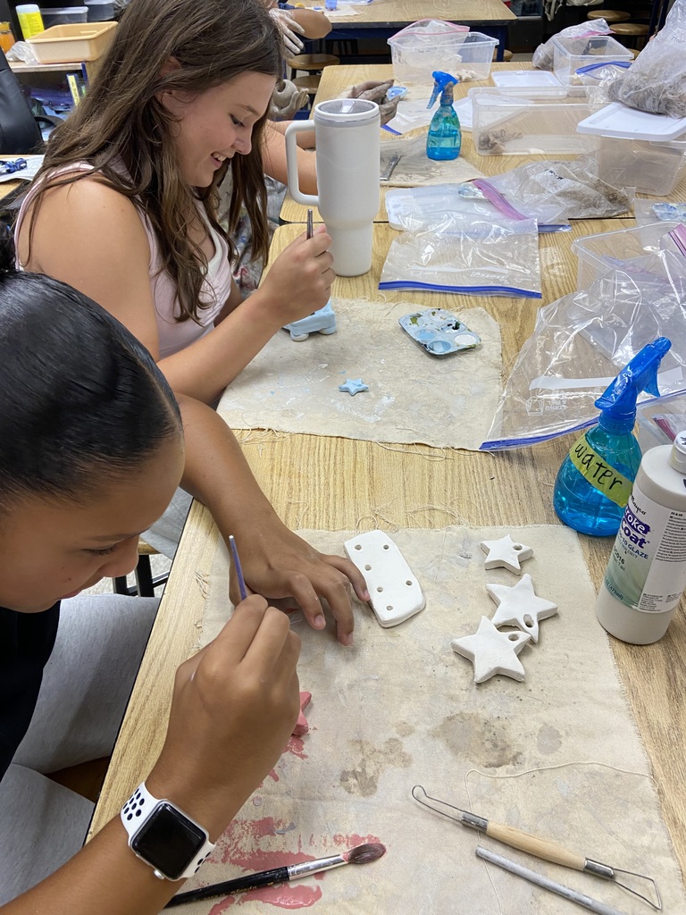 Students painting ceramic ornaments and decorative clay pieces at a classroom table.