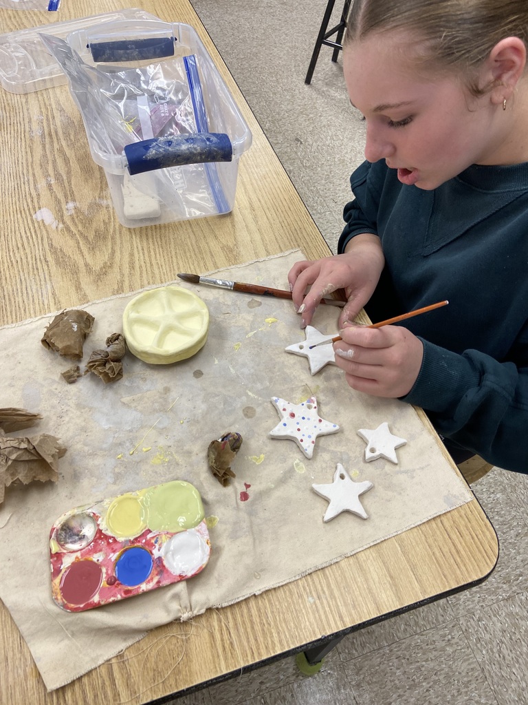 Student painting ceramic star ornaments and a starfish-shaped dish at a classroom table.