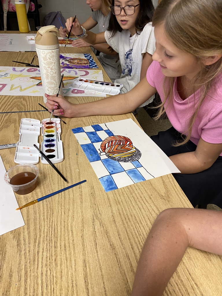 Students painting colorful patterned artwork with watercolors at a classroom table.