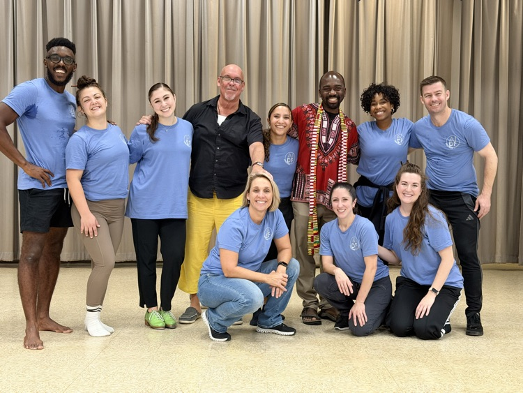 several professional dancers standing on a stage. They are taking a group photo with Mr. Johnson the ElH music teacher. All the adults are smiling.
