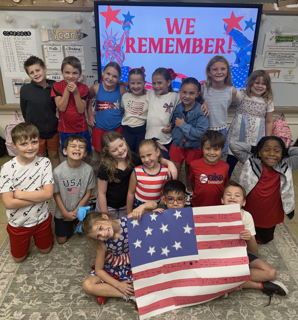 Elementary students holding a handmade flag with the word "We Remember " behind them.