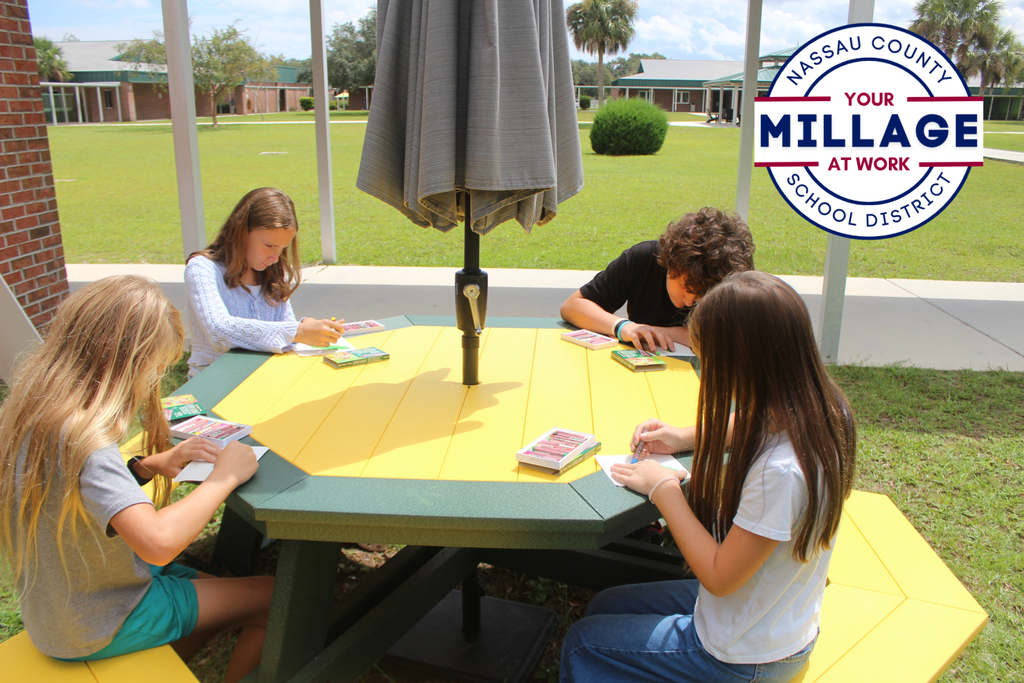 four students are drawing at an outdoor table