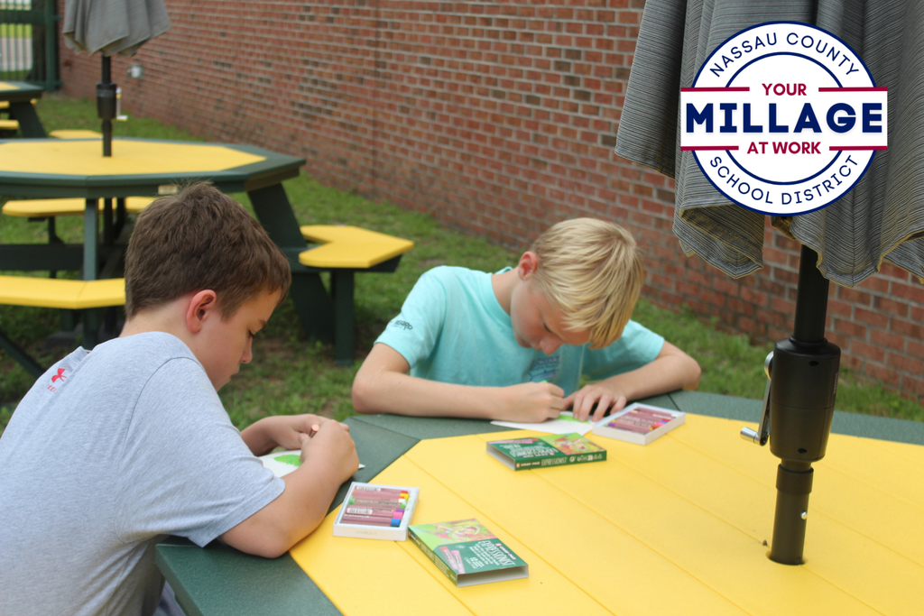 two students are drawing at an outdoor table