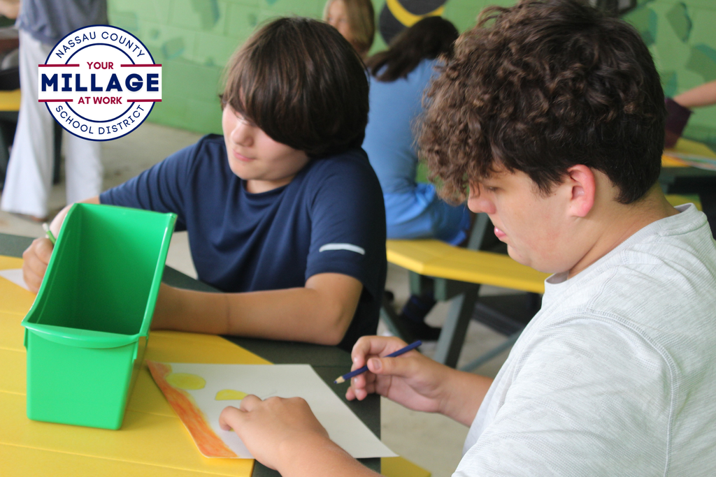 two students are drawing at an outdoor table