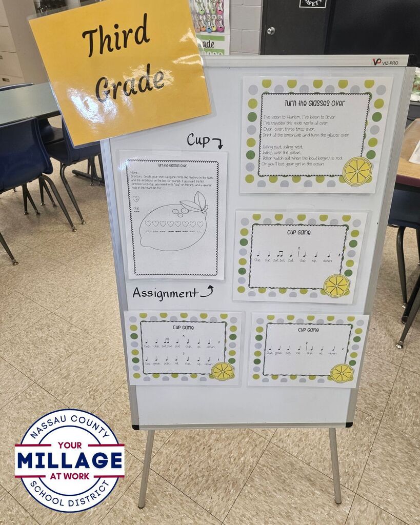 A display board in a music classroom showcases a third-grade music activity. The board includes directions, a song titled “Turn the Glasses Over,” cup rhythm patterns, and a related student assignment. Classroom chairs and tables are visible in the background.