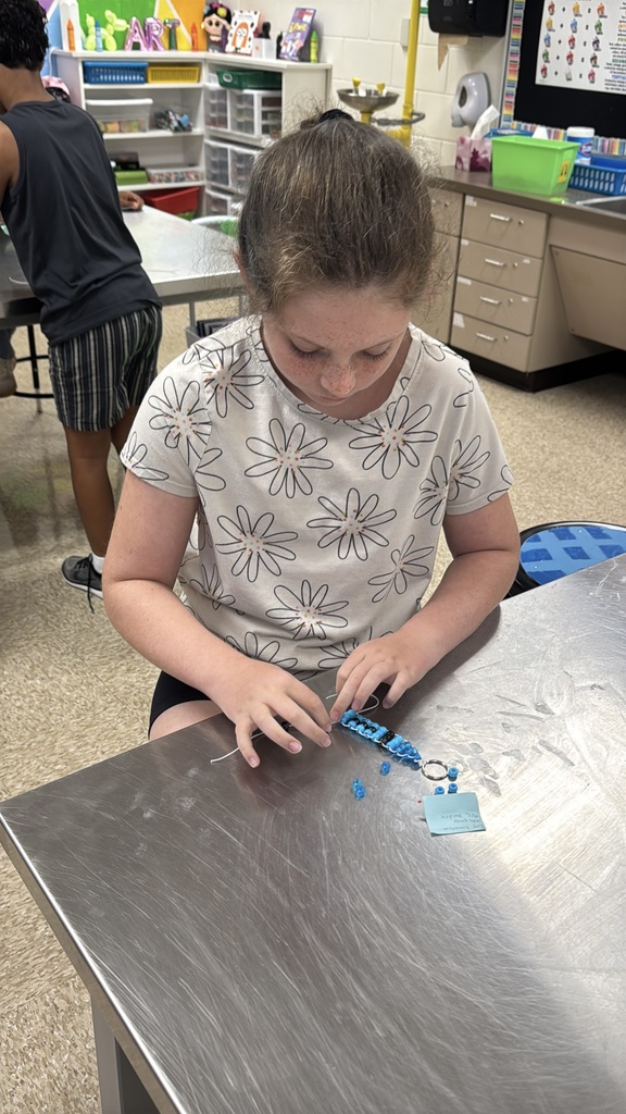 A fourth-grade student carefully weaves blue beads onto string to create a handmade keychain during an art class.