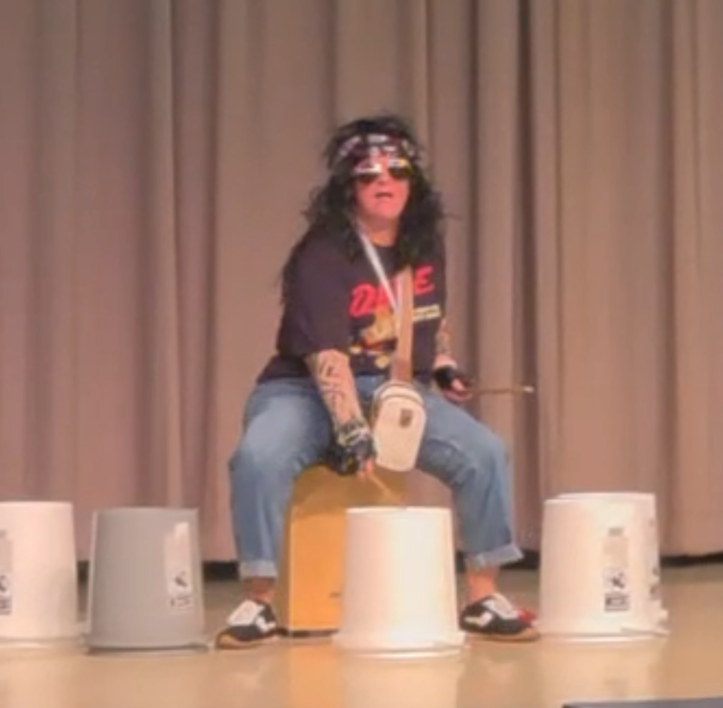 Ms. Domingo playing 5 gallon bucket drums dressed as a rock star. 