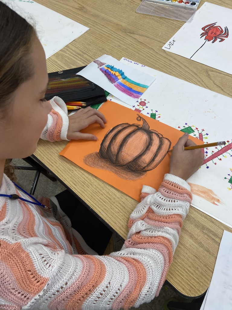 Student making a pumpkin drawing on orange paper.