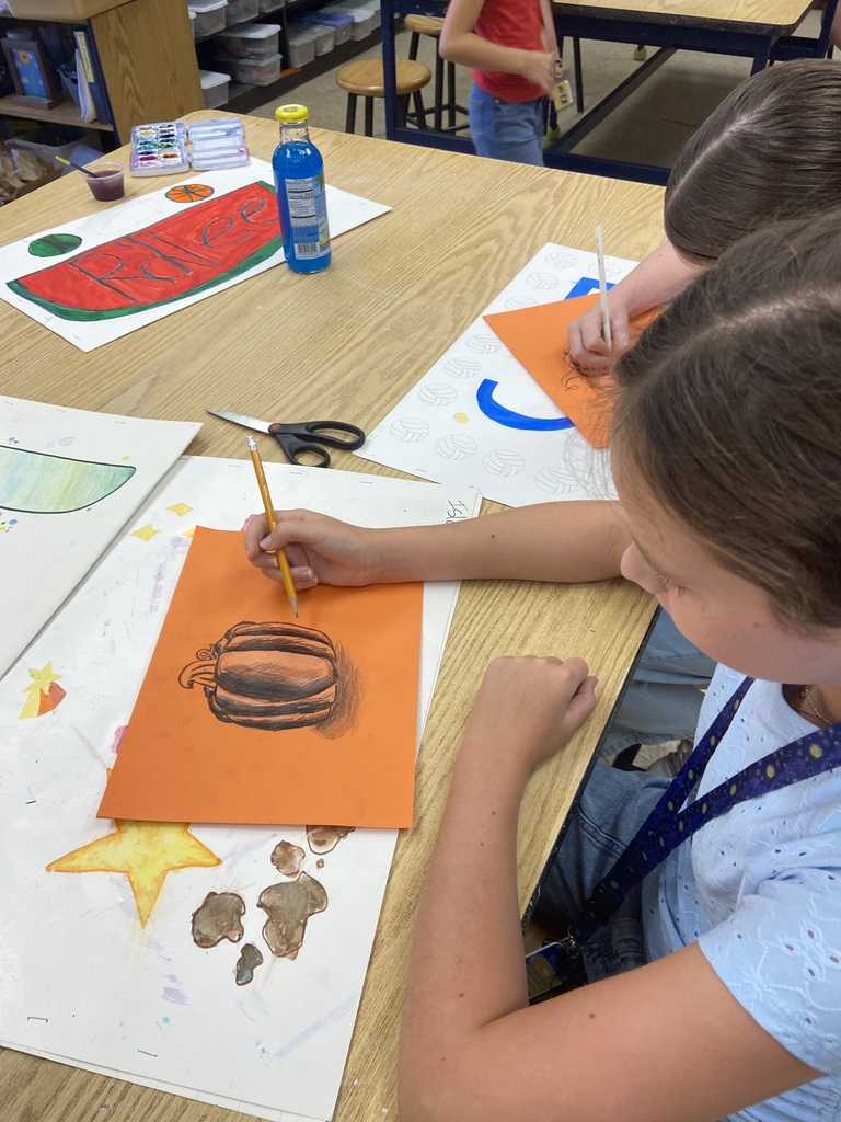 Student making a pumpkin drawing on orange paper.