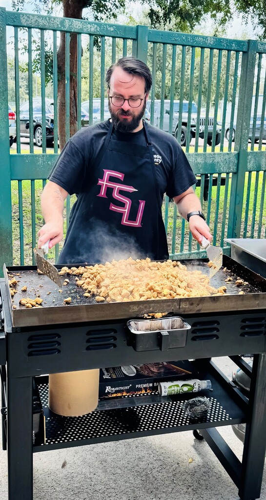 man in apron cooking chicken on a flat top grill