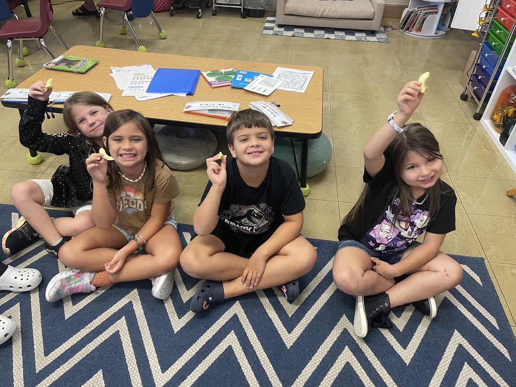a group of students sitting on a blue and white carpet holding up an apple slice