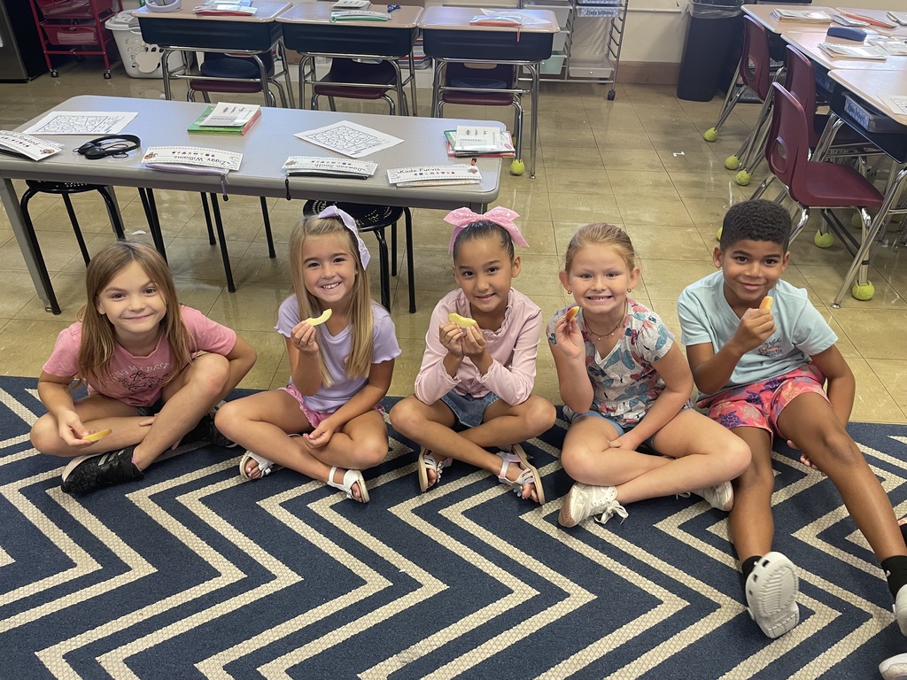 a group of students sitting on a blue and white carpet holding up an apple slice
