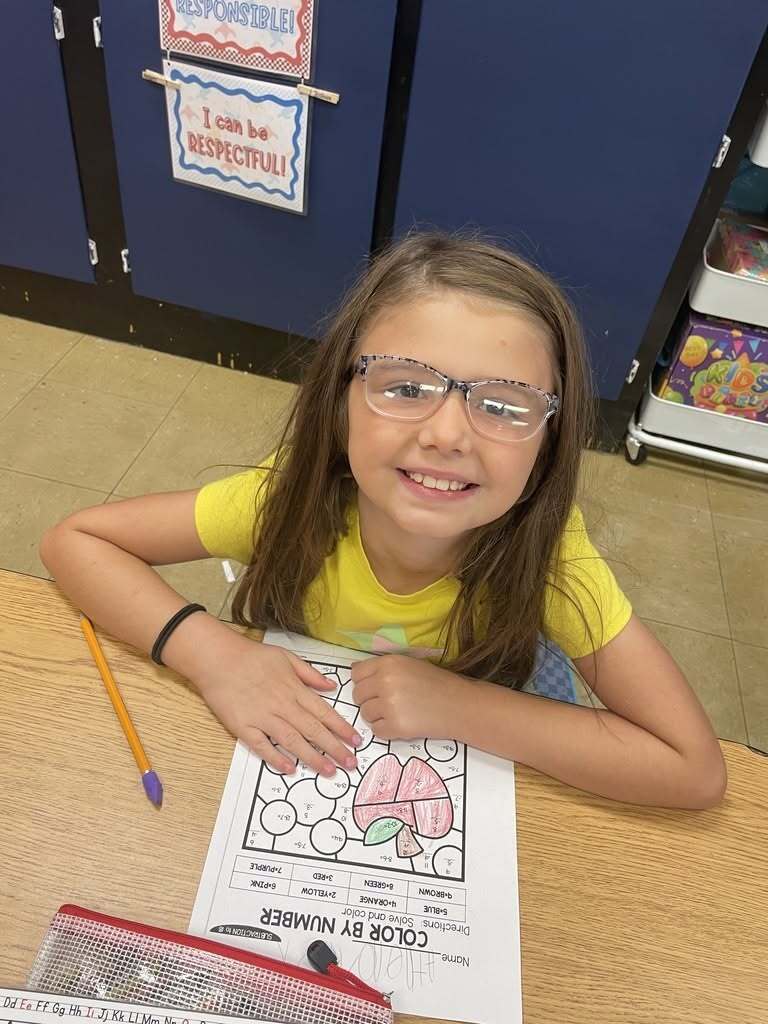 A first-grade student at Callahan Elementary School smiles while completing an apple-themed math activity during Apple Day.