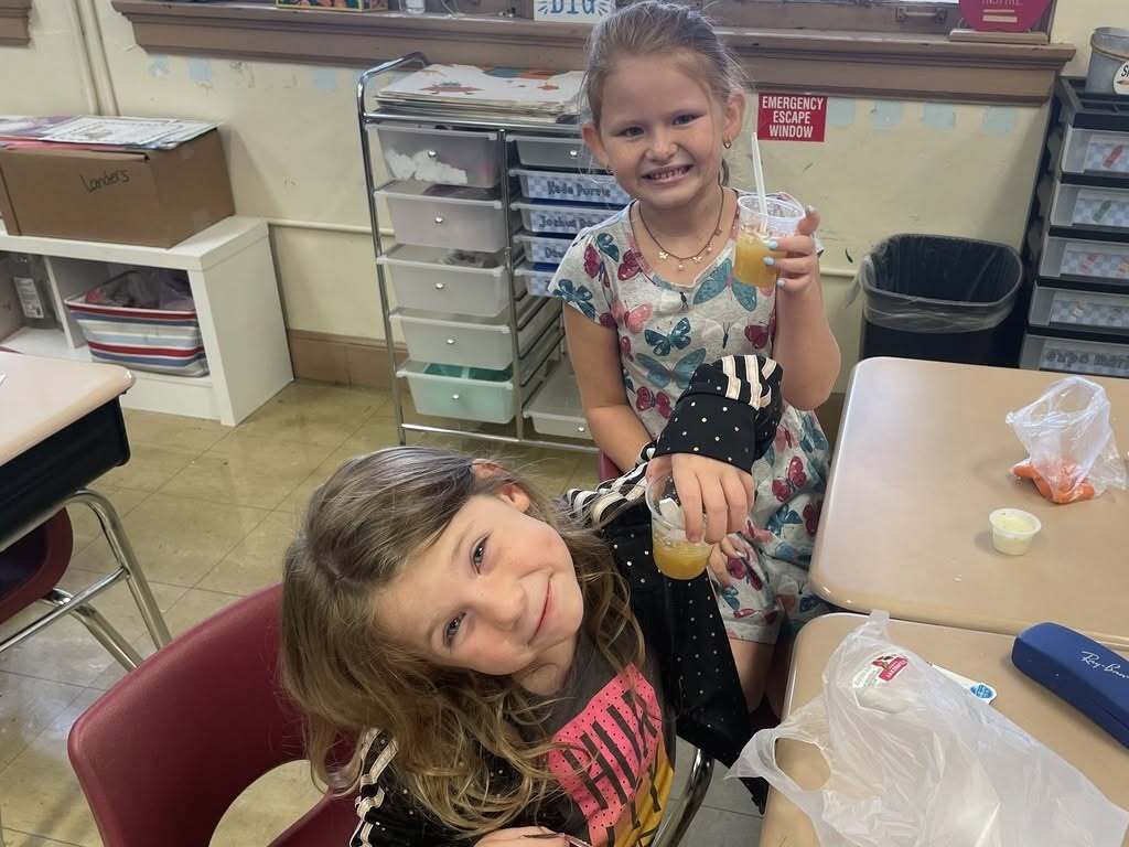 Two first-grade students at Callahan Elementary School smile with cups of homemade applesauce during their classroom Apple Day activities.