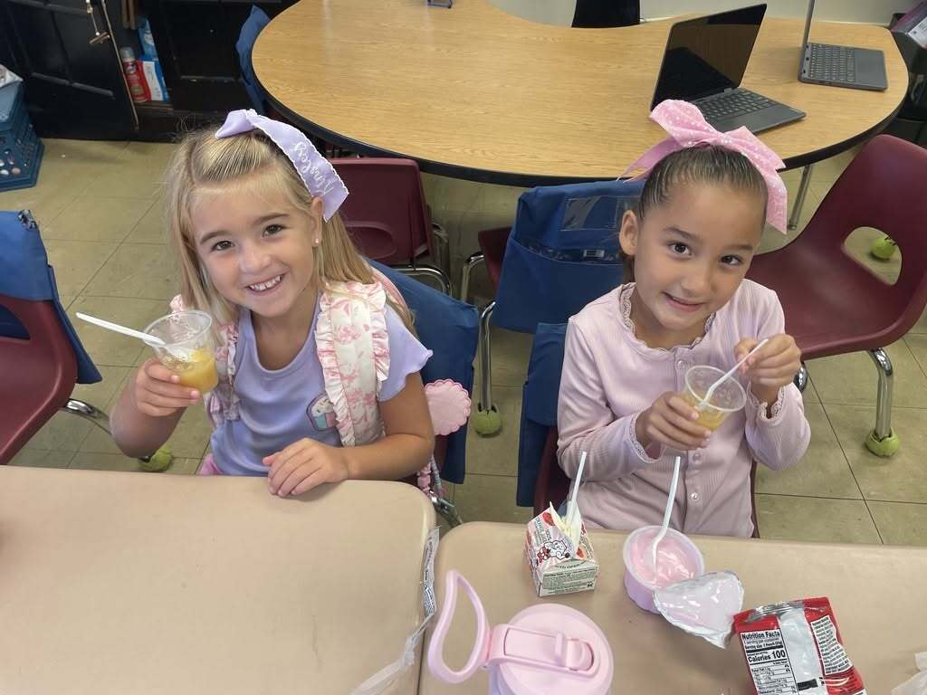 Two first-grade students at Callahan Elementary School taste homemade applesauce as part of an Apple Day lesson combining sensory exploration and hands-on learning.
