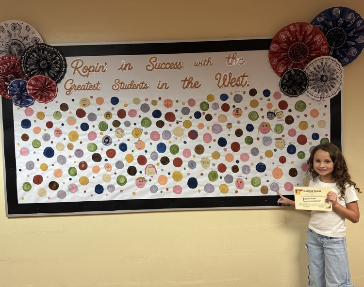  A student proudly points to their self-portrait dot after receiving Warrior Praise for being Respectful, Responsible, and Safe. 