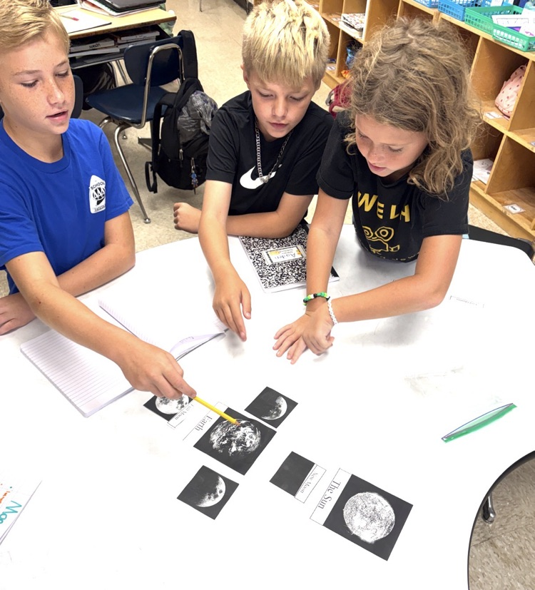3 students working together while pointing at the phases of moon cards
