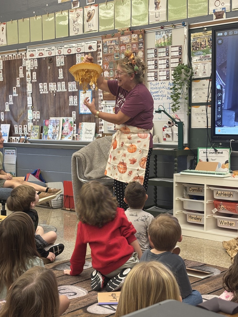 teacher holding up the cut off top of the pumpkin showing students the strands