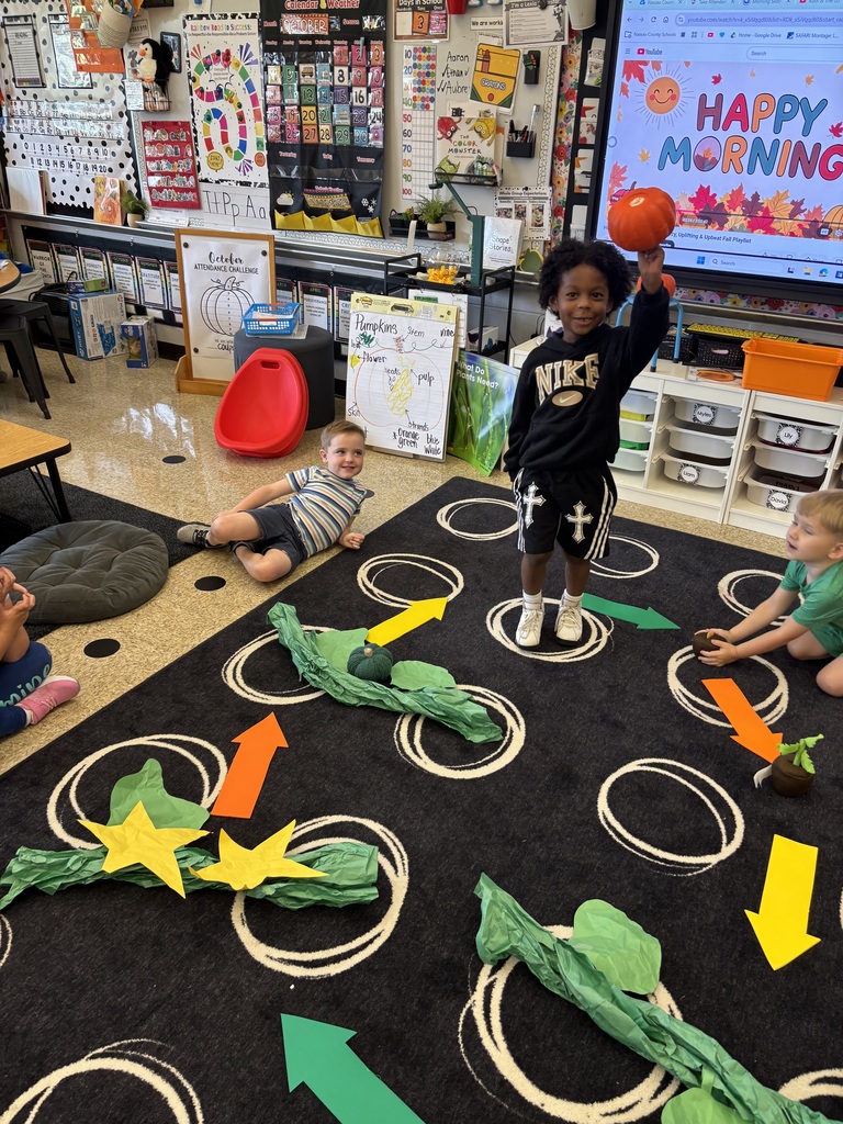 A student standing on a carpet holding up a pumpkin