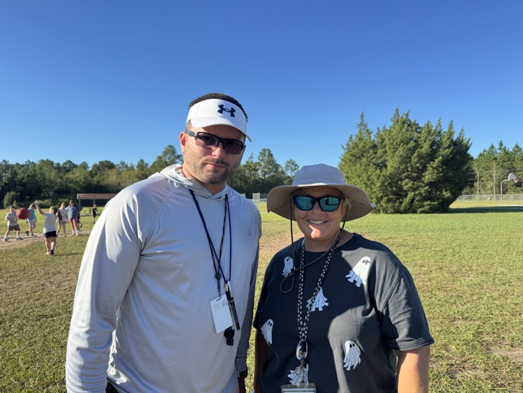 Coach Crews and Ms. Liby smiling for a picture outside during PE.