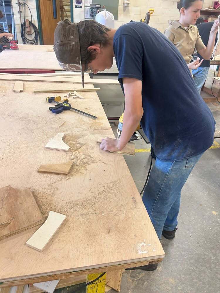 Student works at a large shop table measuring and preparing pieces of wood during a Building Construction class at Yulee High School.