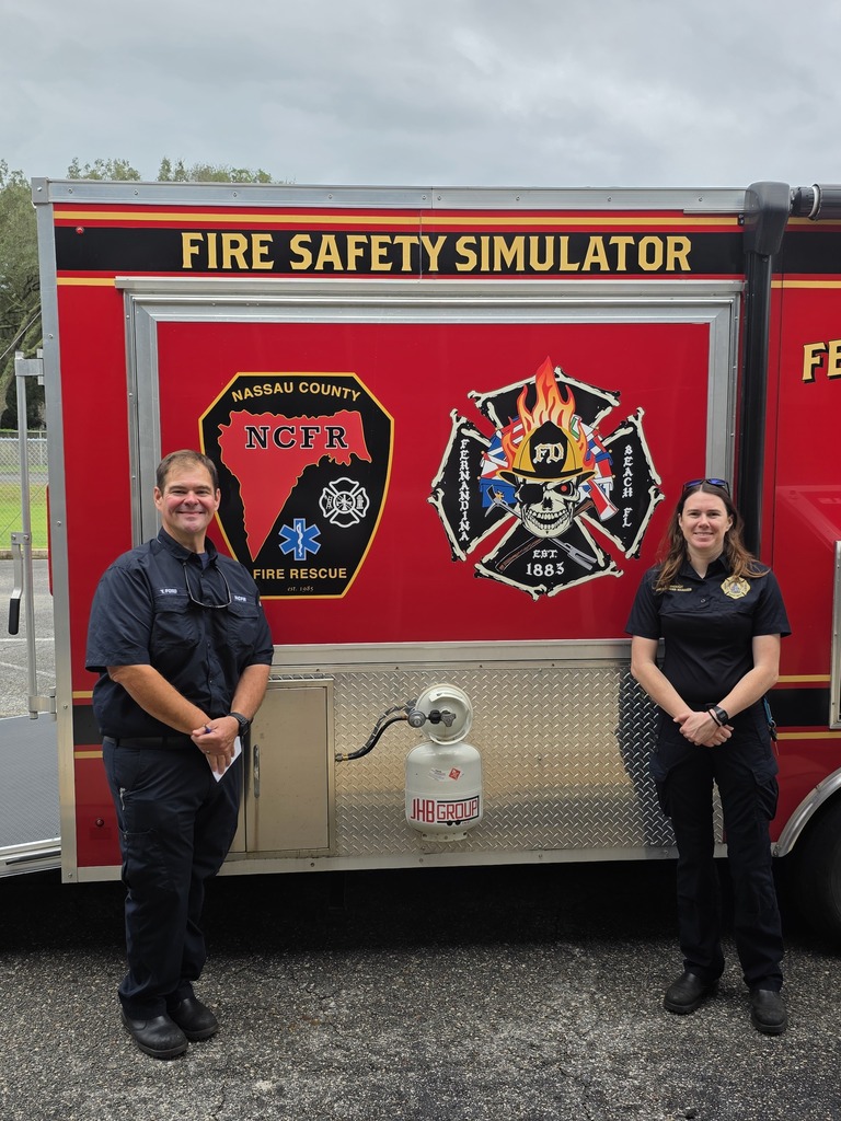 Two firefighters stand in front of the fire simulator.
