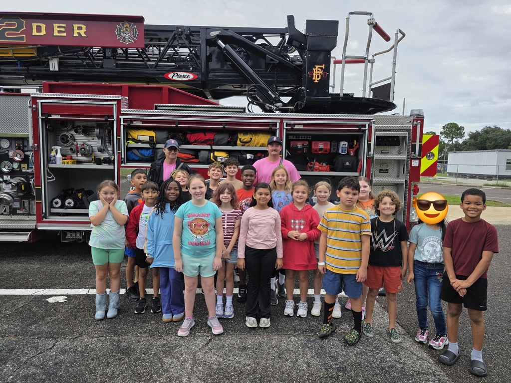 Students stand with two firefighters in front of the fire truck.