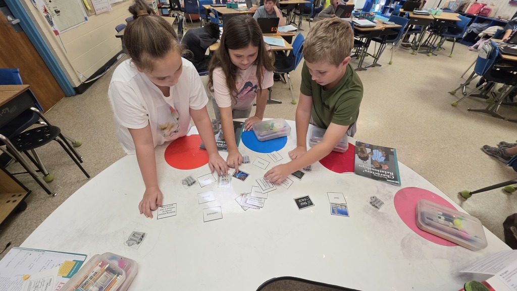Three students are working together to sort and match vocabulary words and definitions.  It is one boy and 2 girls.  