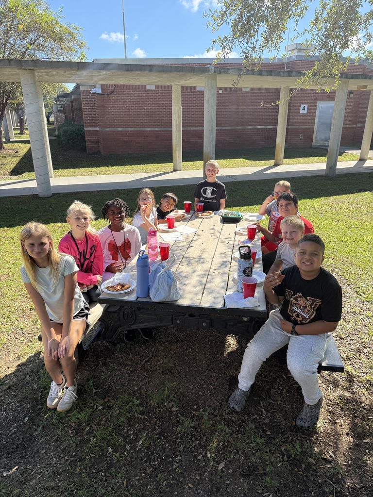 Students enjoy a pizza lunch at outdoor picnic tables under a shady tree to celebrate being among the top five Accelerated Reader (AR) point earners in their grade level.
