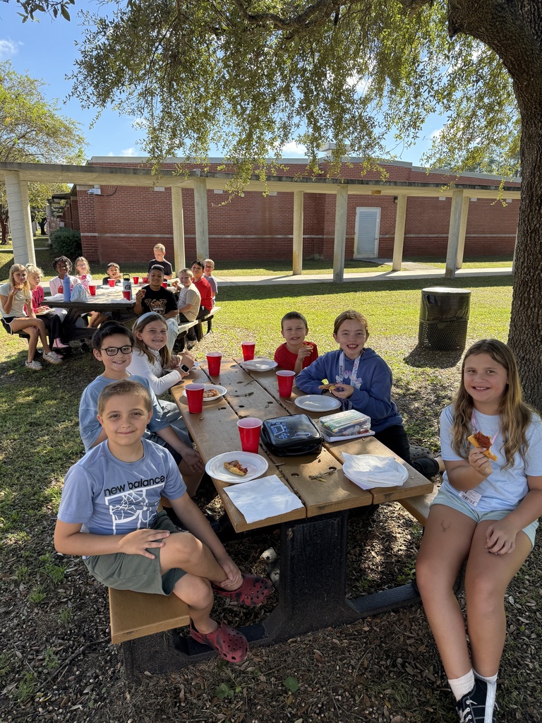 Students enjoy a pizza lunch at outdoor picnic tables under a shady tree to celebrate being among the top five Accelerated Reader (AR) point earners in their grade level.