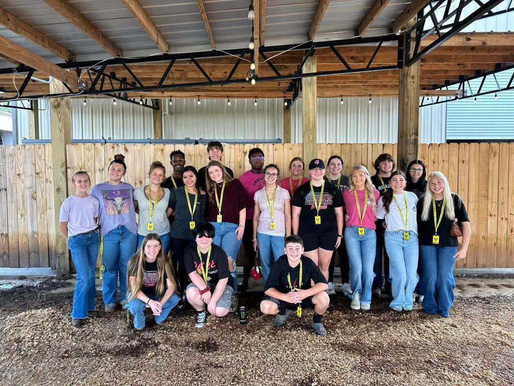 Hilliard Middle Senior High School FBLA students and staff pose together under a covered wooden pavilion at the Northeast Florida Fair. Many of the students are wearing yellow volunteer lanyards while participating in community service at the fair’s Peaceful Patch sensory-friendly experience.