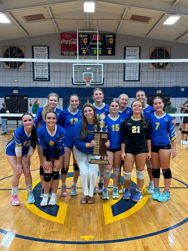 Lady Pirates volleyball team holding a trophy and posing in front of a volleyball net.