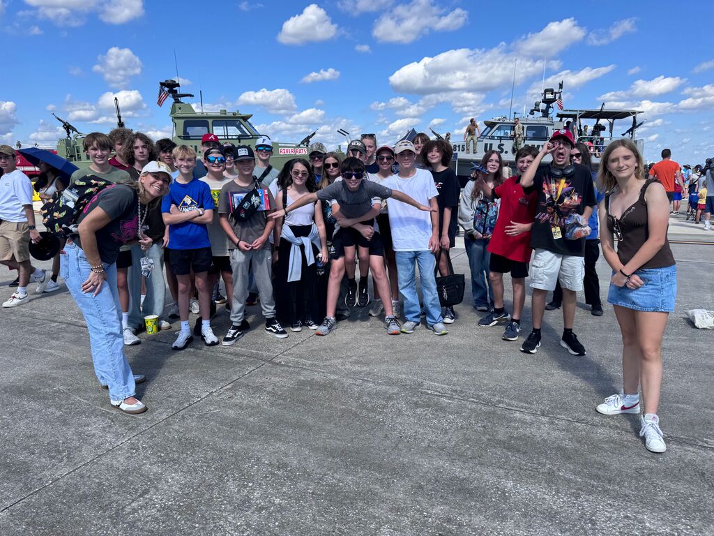 A group of students posing in front of military vehicles.