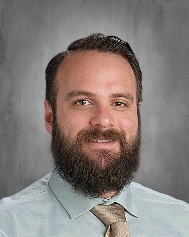 Man with bead looking towards camera with gray background