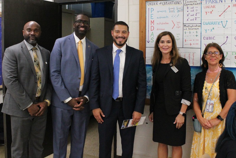 The Commissioner of Education stands with district leaders and middle school teachers inside a math classroom, in front of a bulletin board featuring the order of operations.