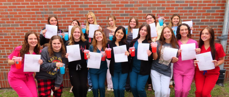 CNA students stand outside holding papers and drinks, smiling and celebrating after completing program requirements.
