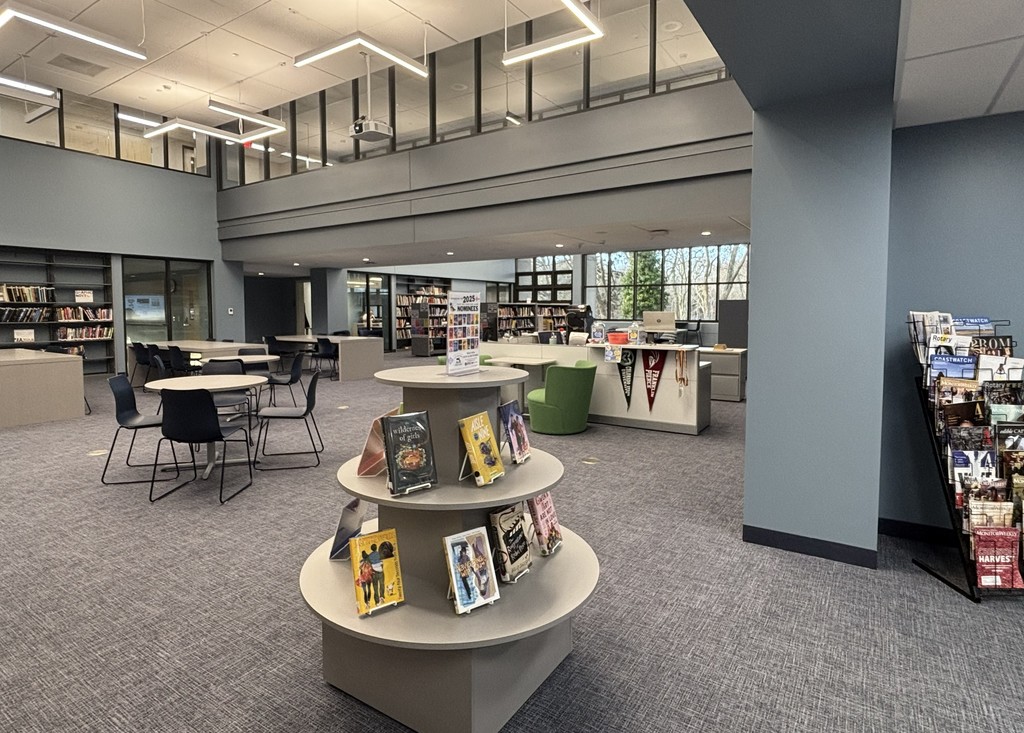 Image of the NRHS Library with book shelves, a magazine rack, tables and chairs