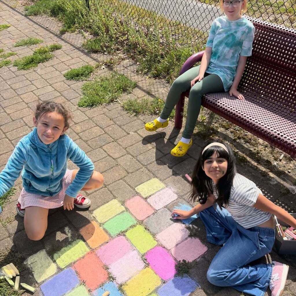 three students draw with chalk on playground